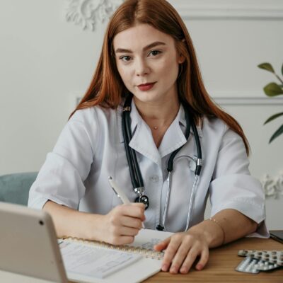 Portrait of a young female doctor with stethoscope, taking notes at her desk with an electronic tablet.