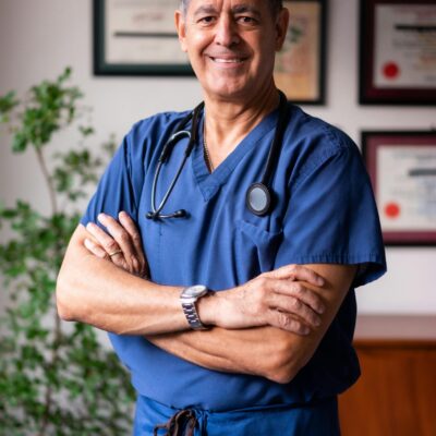 Smiling male healthcare professional in blue scrubs with arms crossed indoors.